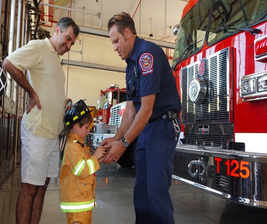 Firefighter helping a young child with a helmet beside a fire truck